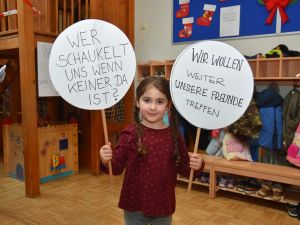 Das Bild zeigt ein kleines Mädchen, dass zwei Schilder hoch hält.