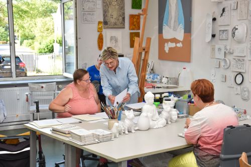 Das Bild zeigt eine Gruppe von Künstlerinnen und der Vereinsvorsitzenden im Atelier Blau, die gemeinsam an ihren Arbeiten sitzen und sich austauschen.
