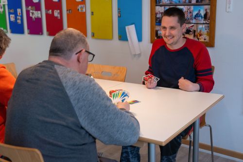 Das Bild zeigt zwei Bewohner beim Kartenspielen in einem farbenfroh gestalteten Gruppenraum des Wohnhauses Samuelstraße.