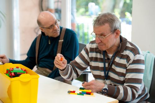 Das Bild zeigt zwei Männer beim konzentrierten Bauen mit Legosteinen an einem Tisch im Wohnhaus Mittendrin.