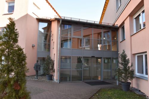 Das Bild zeigt die moderne Glasfassade des Wohnhauses Mittendrin mit seinem barrierefreien Haupteingang.