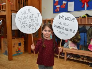 Das Bild zeigt ein kleines Mädchen, dass zwei Schilder hoch hält.