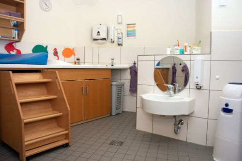 Das Bild zeigt einen kindgerecht gestalteten Waschraum mit Wickeltisch, Waschbecken und bunten Wandmotiven.